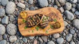 Fire-grilled swordfish steak sliced open on a wooden board with herb oil drizzle and charred lemon halves